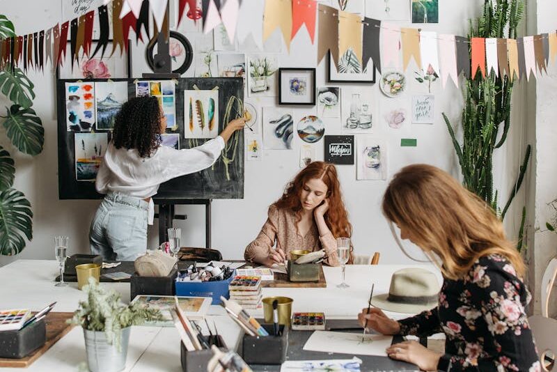 Artists paint in a bright, creative studio adorned with artwork and plants, fostering a vibrant atmosphere.